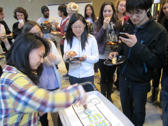 Bob sneaks a picture right before Elaine cuts the class cake.